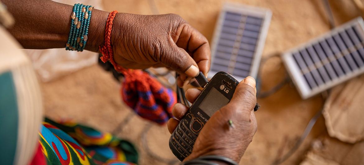 زنی در اردوگاه آوارگان در بورکینافاسو از انرژی خورشیدی برای شارژ تلفن همراه خود استفاده می کند.